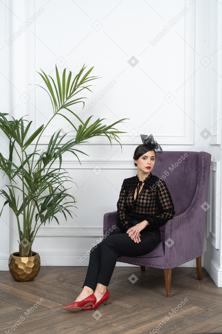 Elegant woman in blouse sitting in armchair next to houseplant