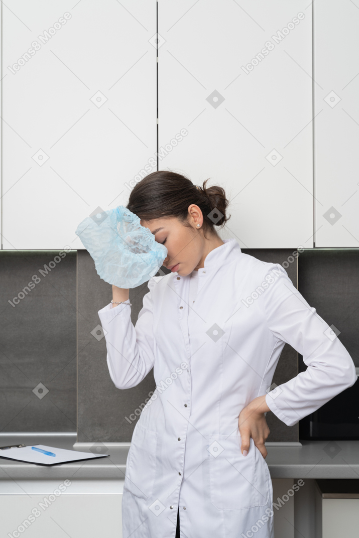 Front view of a tired female doctor touching head