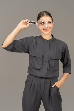 Front view of a smiling young woman in a jumpsuit holding a magnifying glass