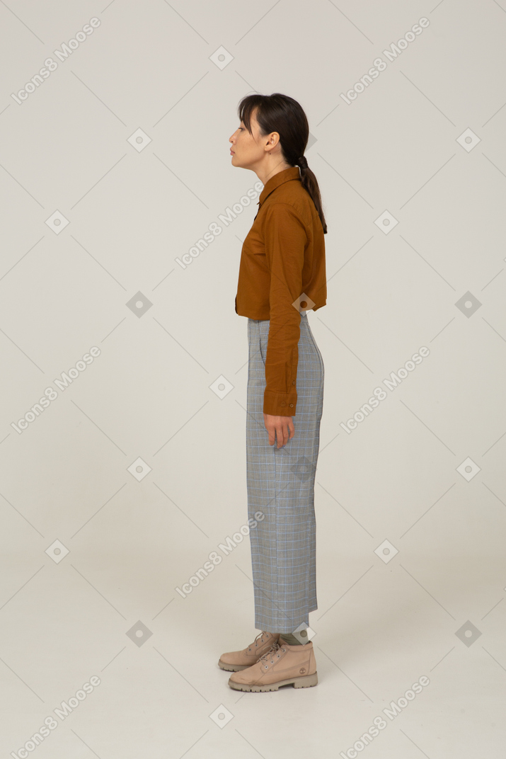 Vista laterale di una giovane donna asiatica in calzoni e camicetta in piedi ancora
