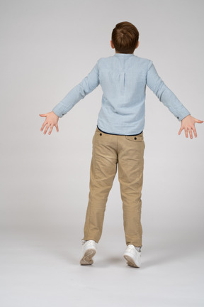 Back view of a boy standig on tiptoes with his arms outstretched