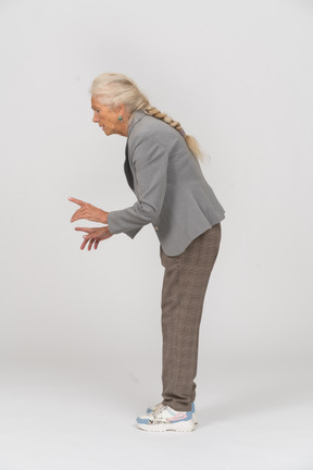 Vista lateral de una anciana en traje agachándose y mostrando la señal de advertencia