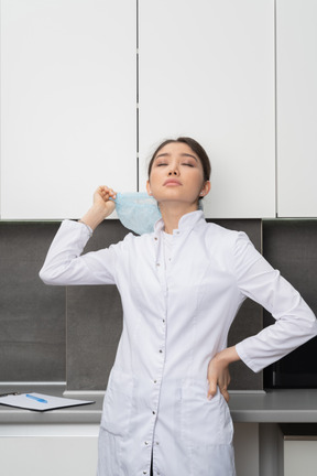 Front view of a tired female doctor raising hand with her eyes closed