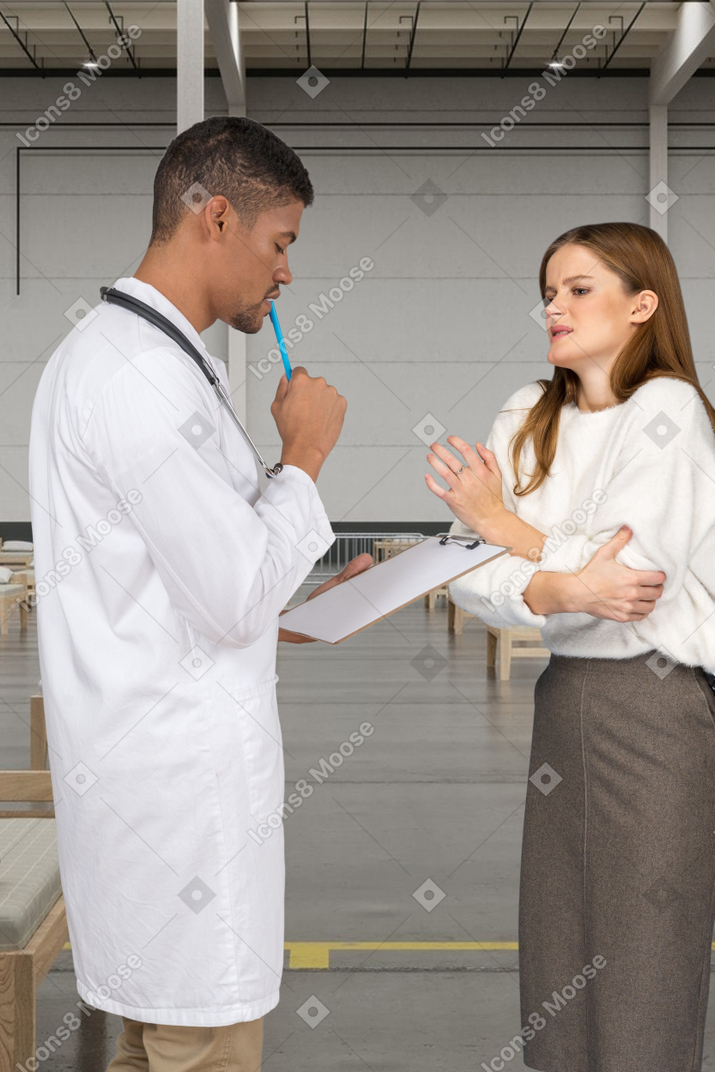A male doctor with clipboard standing next to a female patient