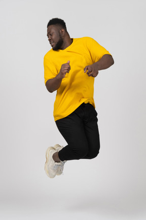 Front view of a jumping young dark-skinned man in yellow t-shirt