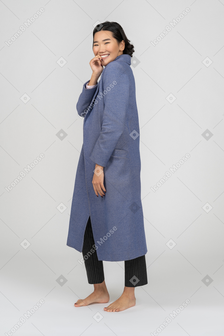 Vista lateral de una mujer sonriente con abrigo azul con la mano al lado de la boca