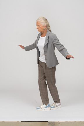 Vista lateral de uma senhora idosa de terno se equilibrando com os braços estendidos