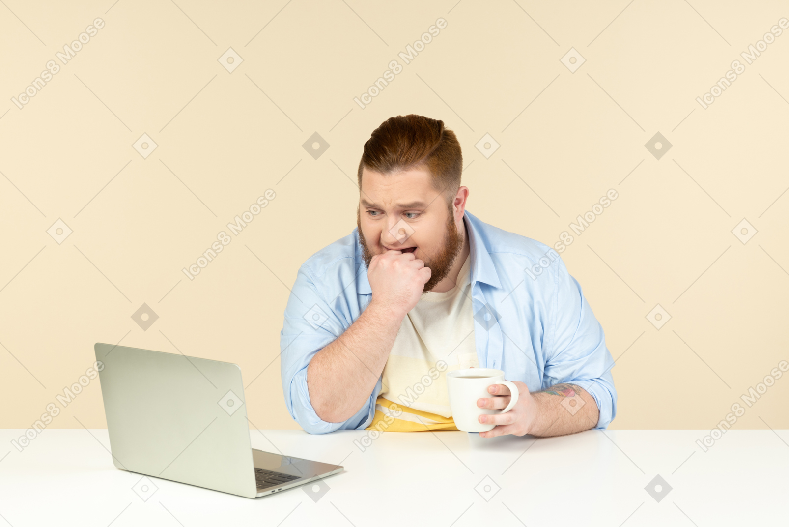 Angry looking young overweight man sitting in front of laptop and having tea