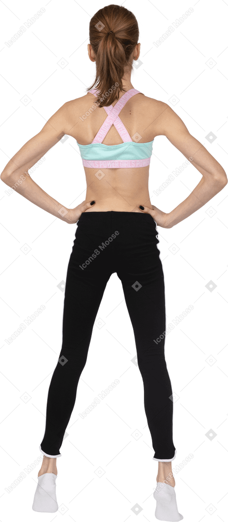Vista posteriore di una ragazza adolescente in abbigliamento sportivo che mette le mani sui fianchi stando in punta di piedi