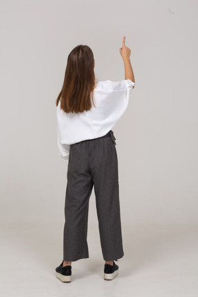 Vista traseira de uma jovem com roupa de escritório apontando o dedo para cima