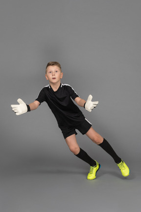 Front view of a kid boy goalkeeper jumping and outstretching hand