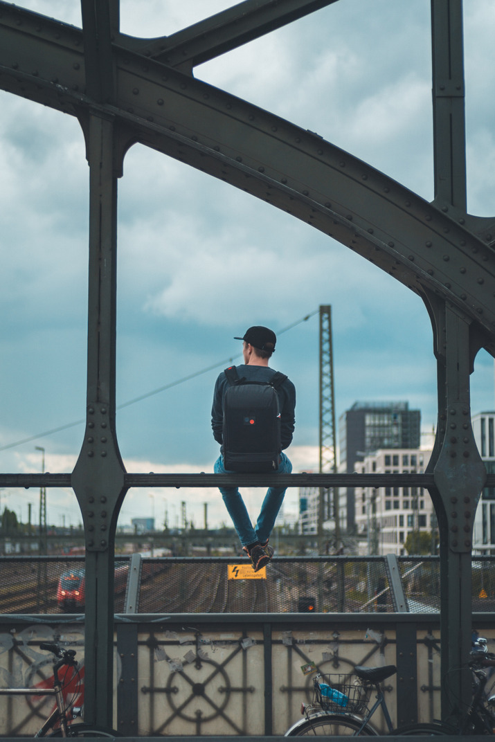 Вид сзади на молодого человека, сидящего на перилах моста