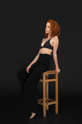 A three-quarter side view of the sexy elegant woman, sitting on the wooden chair and looking to the left