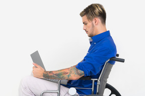 Hombre guapo joven sosteniendo una computadora portátil en una silla de ruedas