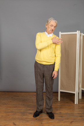 Front view of an old man looking at camera while touching shoulder