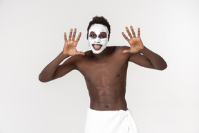 A young black man with a white bath towel around his waist going about his facial care