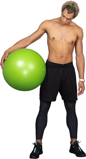 Front view of a shirtless afro man holding a big green gym ball