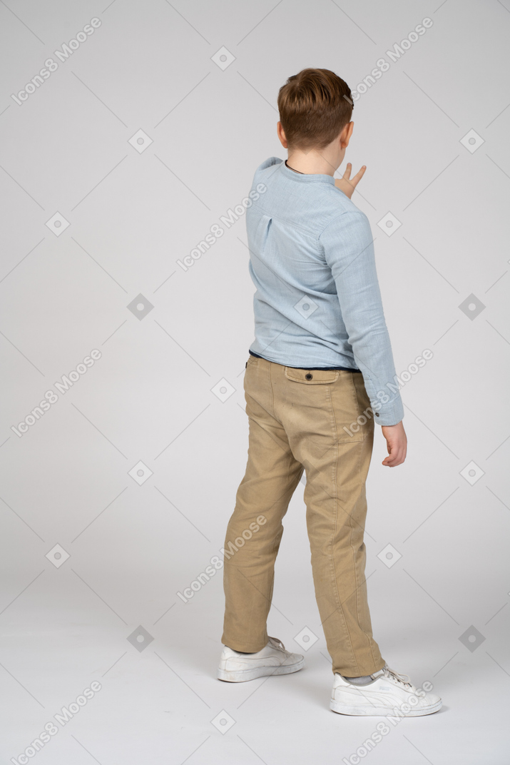 Vista traseira de um menino mostrando sinal de v