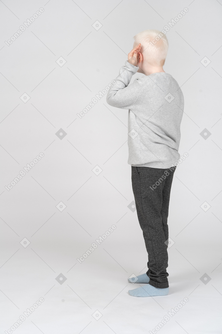 Three-quarter back view of a boy putting palm to his ear