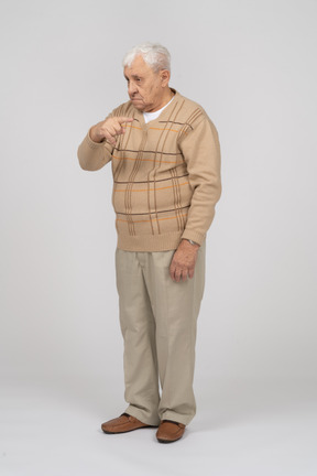 Front view of an old man in casual clothes poinitng with finger