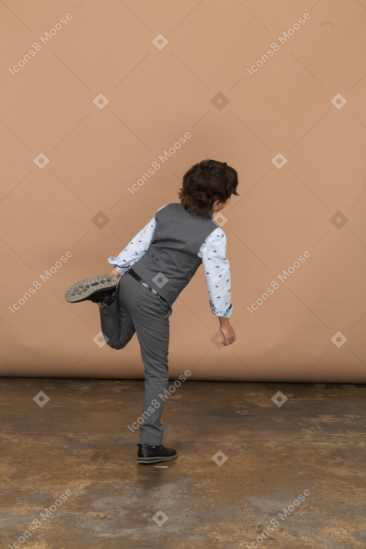 Vista traseira de um menino de terno em pé em uma perna