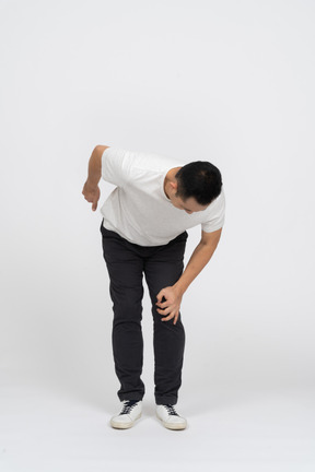 Front view of a man bending down and touching hurting knee
