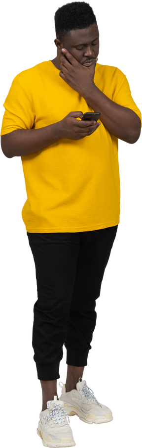 Front view of a young dark-skinned man in yellow t-shirt chatting via phone
