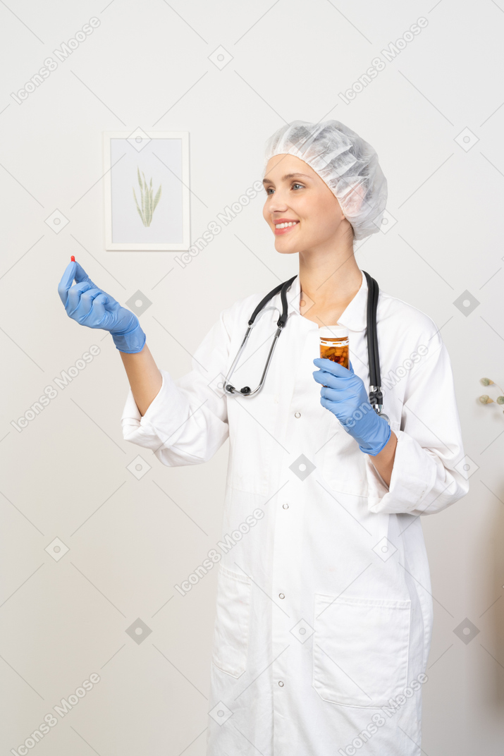 Three-quarter view of a smiling young female doctor offering a pill