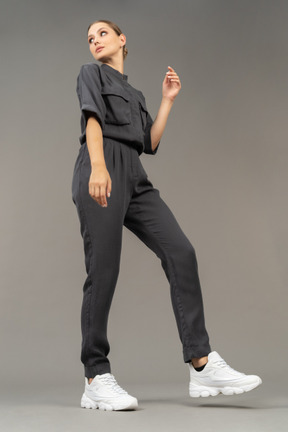 Side view of a bossy young woman in a jumpsuit looking aside & raising hand