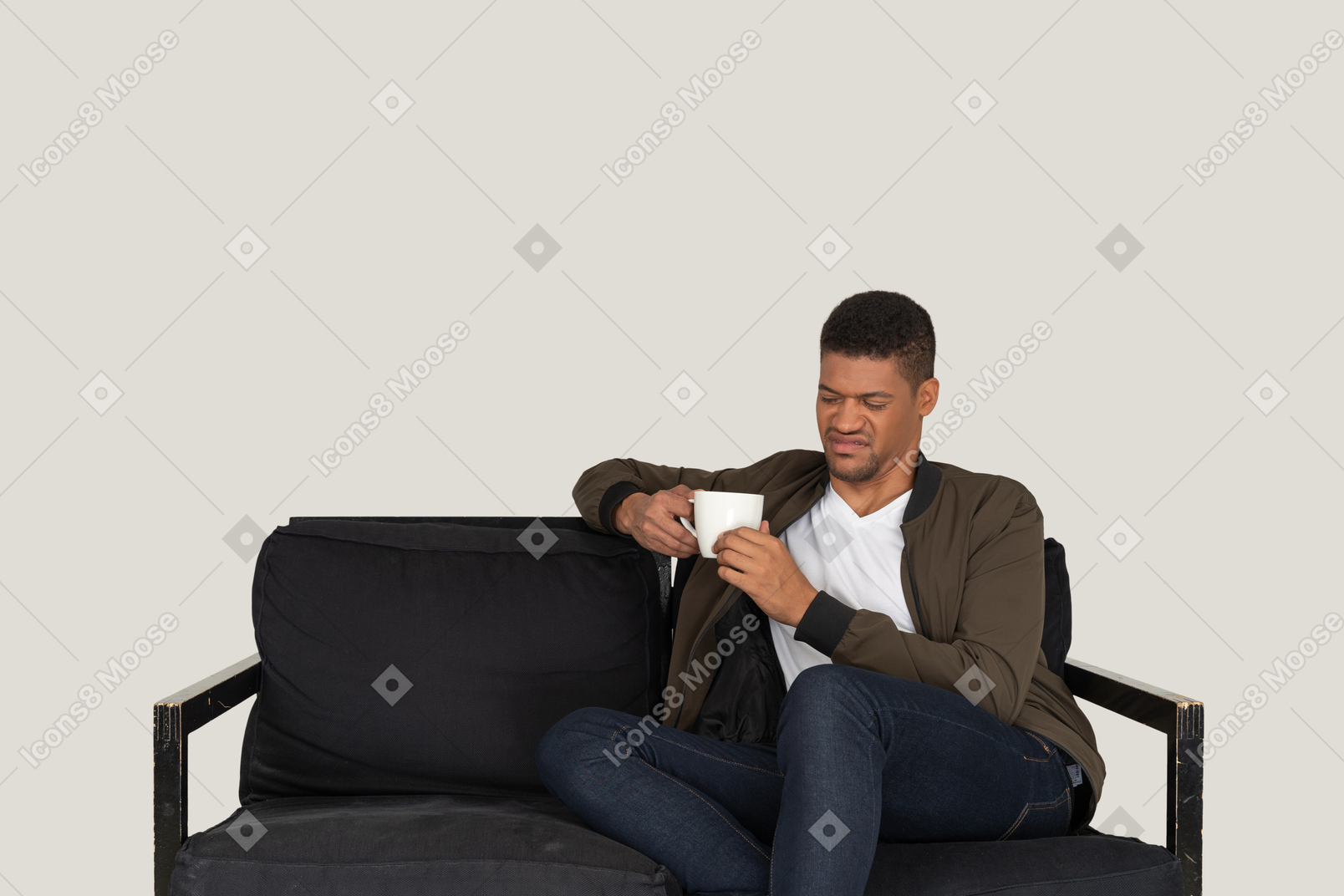 Front view of a young grimacing man sitting on a sofa with a cup of coffee