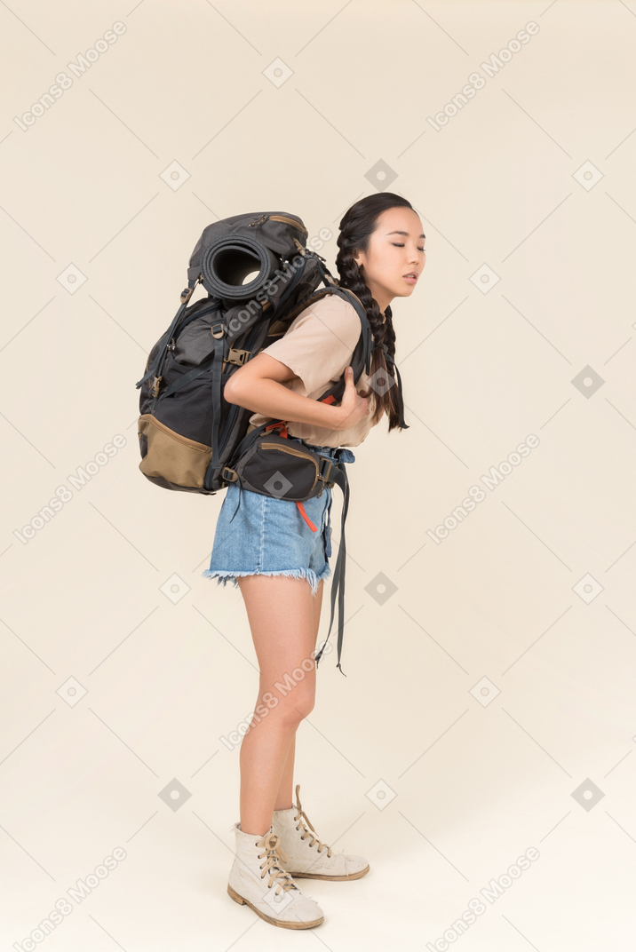 Tired looking female asian hiker standing with huge backpack