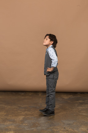 Vista lateral de um menino de terno cinza em pé com as mãos nos quadris