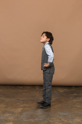 Vista lateral de un niño con traje gris de pie con las manos en las caderas