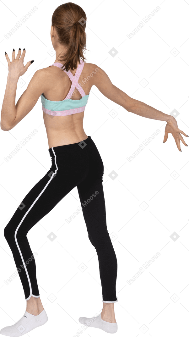 Vista posterior de una jovencita en ropa deportiva levantando las manos y bailando