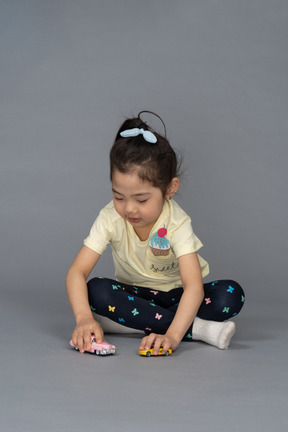 Niña jugando con coches de juguete mientras está sentada en el suelo