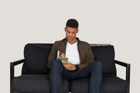 Front view of young man sitting on a sofa and making notes