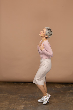 Vista lateral de uma mulher emocional em roupas casuais em pé com as mãos no peito