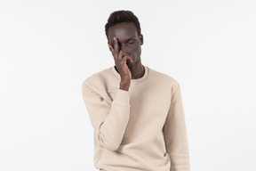 Un joven negro en un suéter gris de pie solo sobre el fondo blanco.