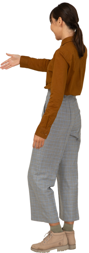 Vista posterior de tres cuartos de un saludo joven mujer asiática en calzones y blusa extendiendo la mano