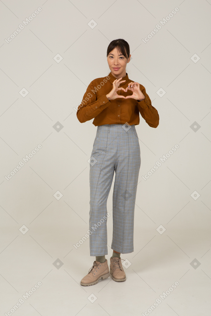 Front view of a young asian female in breeches and blouse showing heart gesture