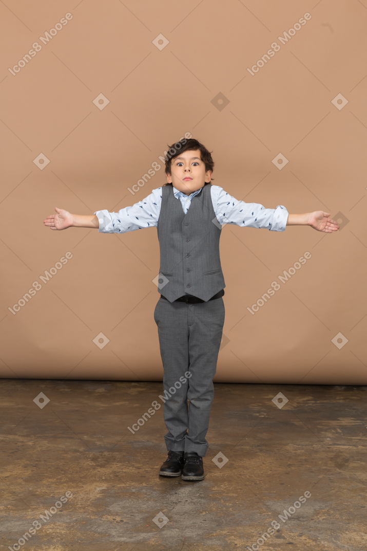 一个穿着西装的可爱男孩张开双臂站立的正面图
