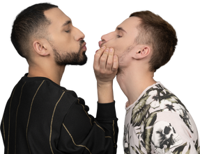 Close-up of a young man holding another man by jaw not too gently as if trying to kiss