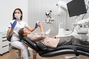 Comprimento total de uma dentista perplexa mostrando a sua paciente um modelo de dentes
