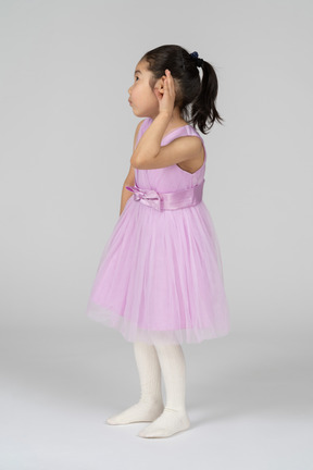 Маленькая девочка в розовом платье пытается что-то услышать