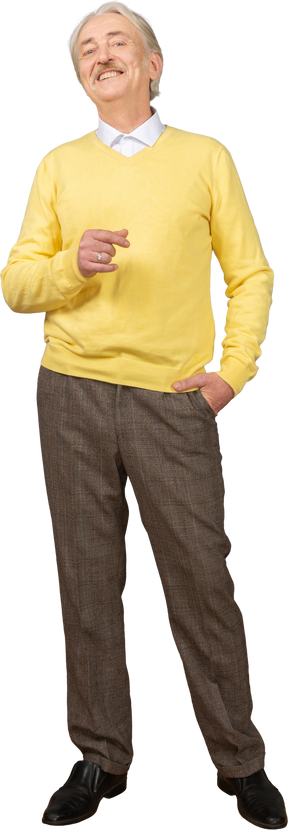 Vorderansicht eines erfreuten lächelnden alten mannes in einem gelben pullover, der hand hebt und kamera betrachtet
