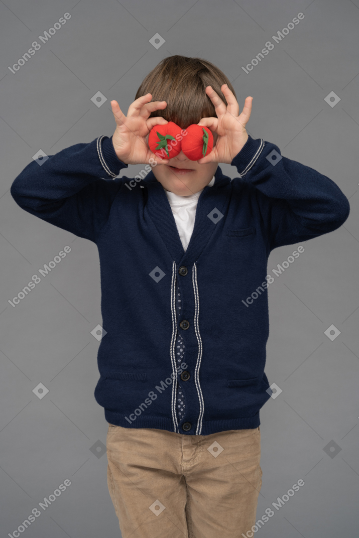 Portrait of a little boy hiding his eyes behind two tomatoes