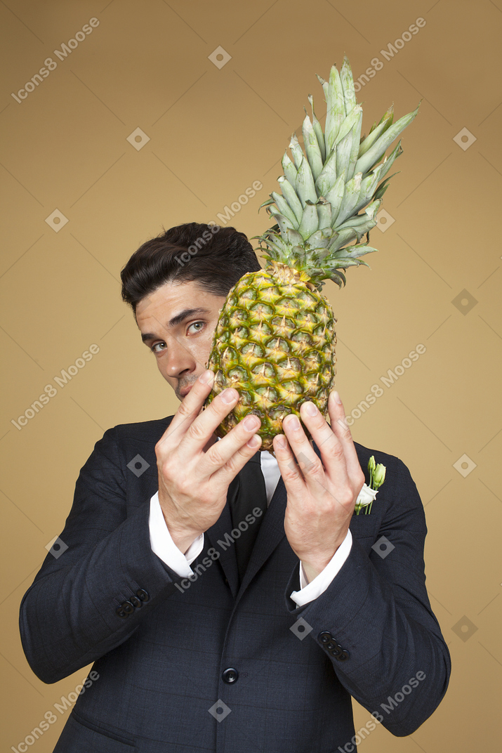Groom in black jacket holding an ananas and closing his face with it