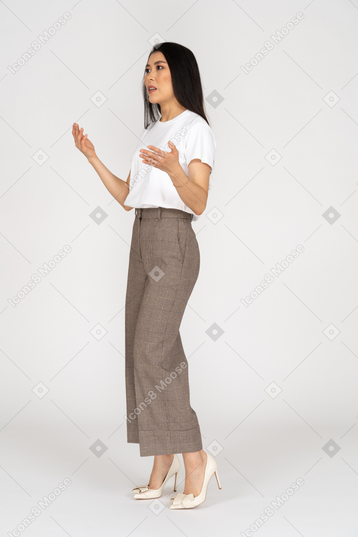 Vista di tre quarti di una giovane donna che discute gesticolante in calzoni e maglietta