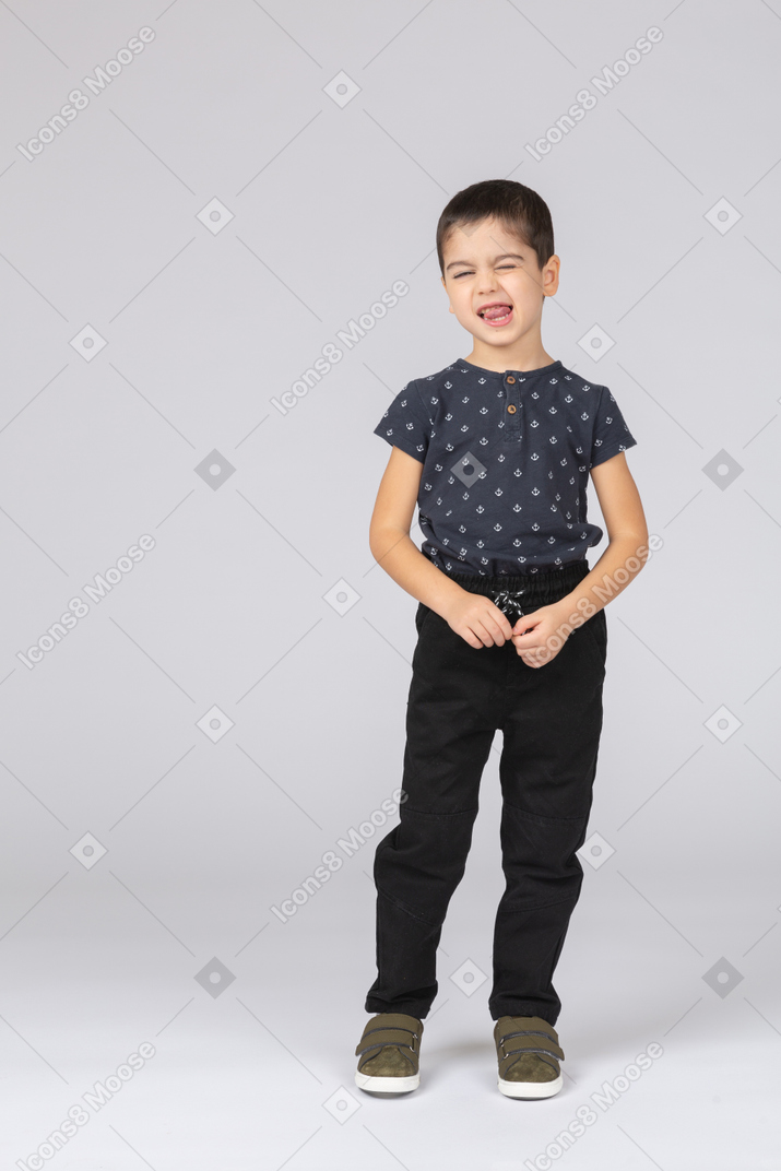 Front view of a cute boy in casual clothes showing tongue and looking at camera