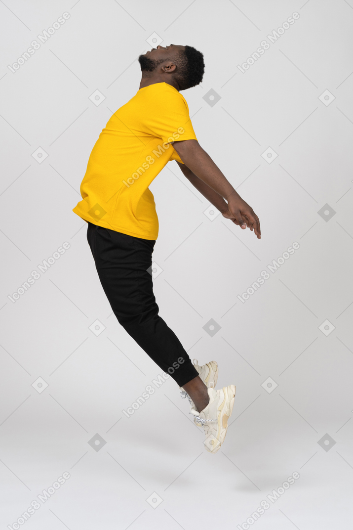 Side view of a jumping young dark-skinned man in yellow t-shirt outspreading hands